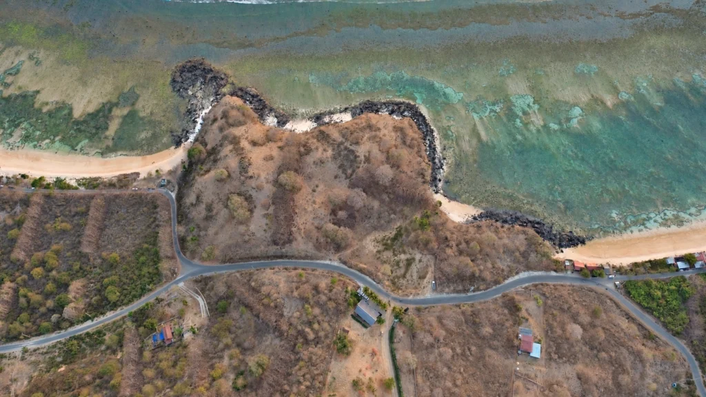 Overhead view of the rocky headland, beach and coastal road at Glampar Beach, Kertasari.
